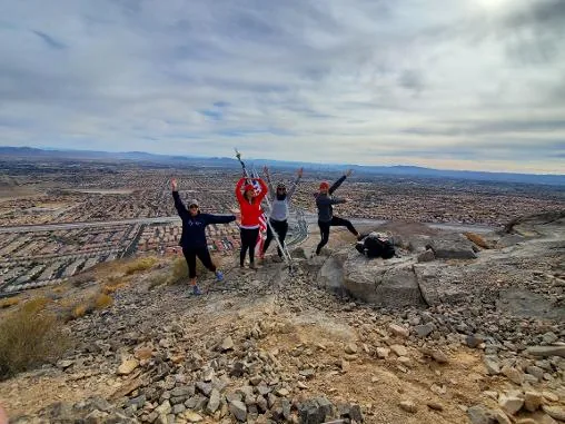 A hiking group jumping and cheering on the Lone Mountain summit above the Las Vegas valley